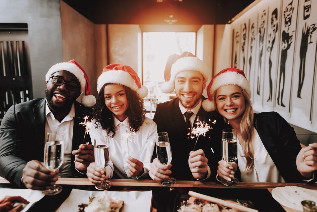 Holiday employee appreciation ideas: co workers posing with champagne and Christmas hats.