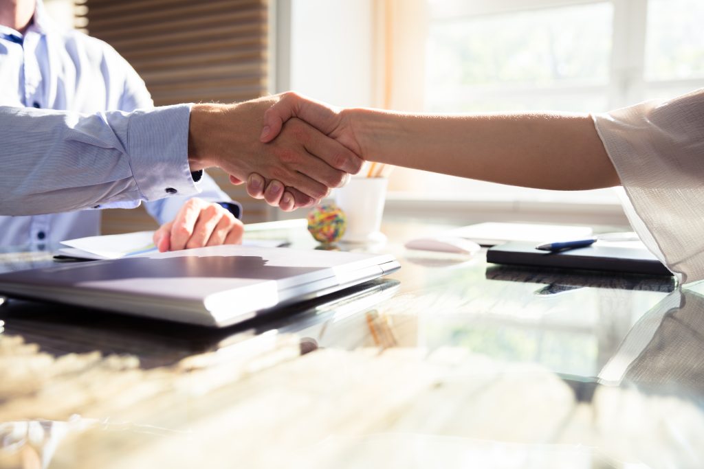 Close-up of two business partners shaking hands over desk in office. 